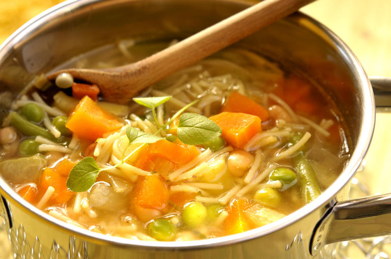 Gemüsenudelsuppe und Holzlöffel im Kochtopf