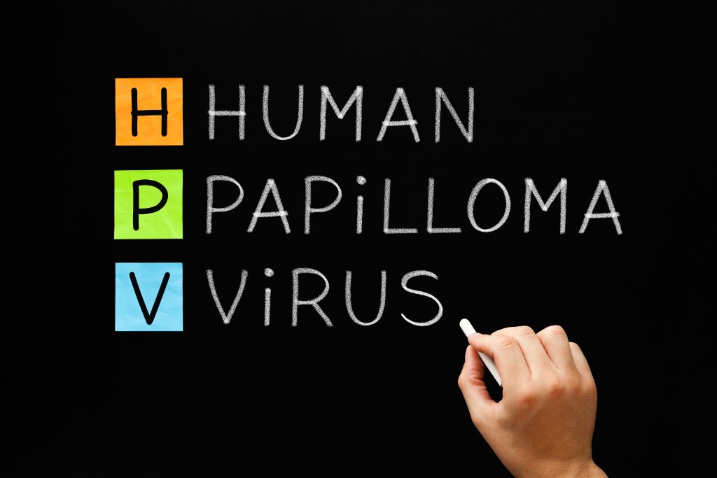 HPV wird farbig hervorgehoben auf einer Tafel geschrieben. Eine Hand hält Kreide.