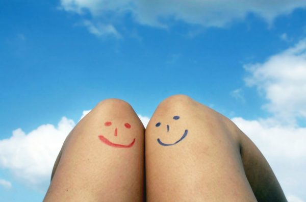 Blick über Frauenbeine mit rotem und blauem Smiley in blauen Himmel