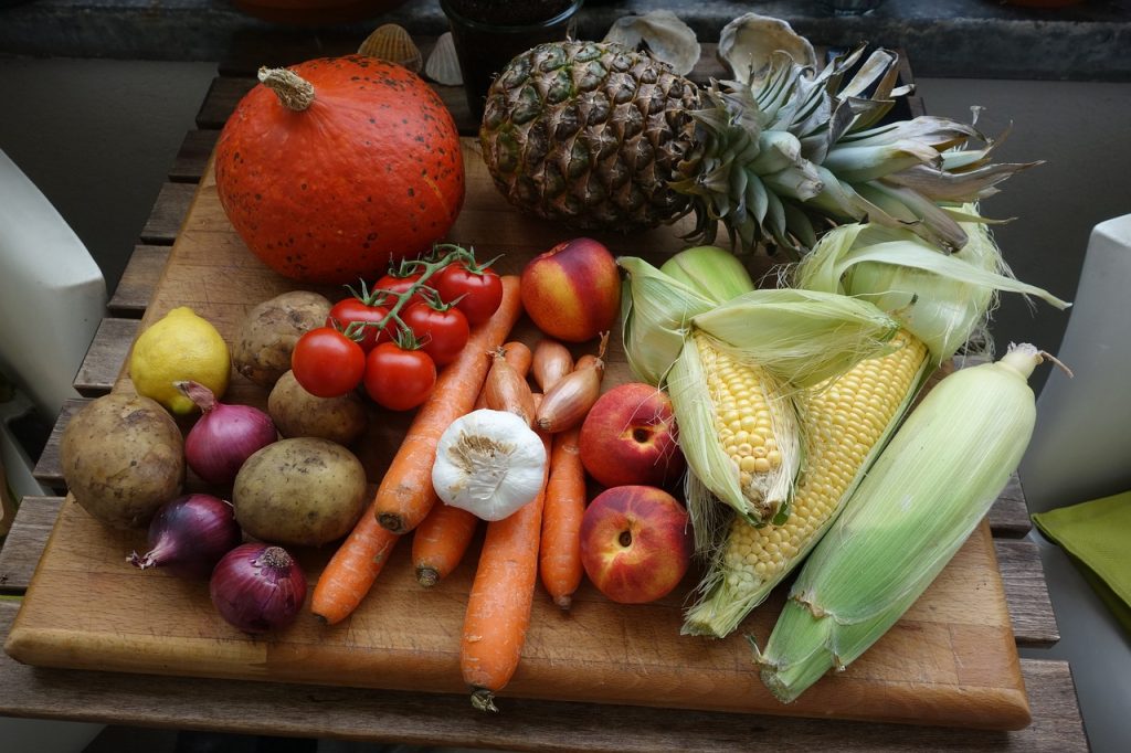 Verschiedene Früchte und Gemüse auf einem Holztisch, darunter Mais, Tomaten und Ananas.
