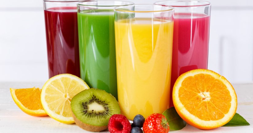 Vier Gläser mit verschiedenfarbigen Säften und frischen Früchten wie Orange, Kiwi und Himbeere.